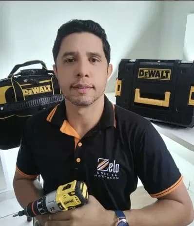 Leandro, fundador e montador da Zelo Móveis, de uniforme e com uma parafusadeira na mão
